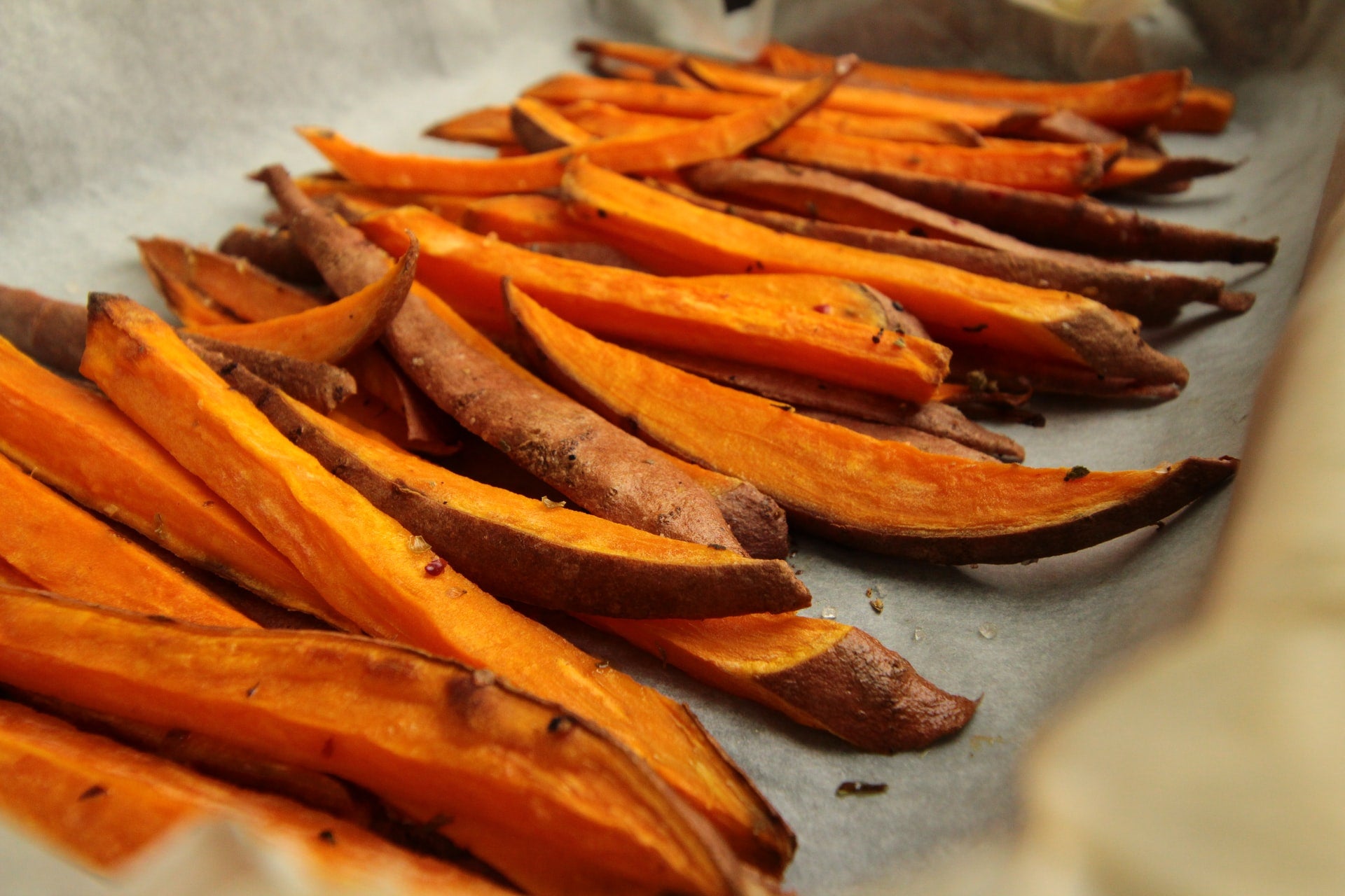 Close-up of sweet potato fries with orange flesh and skin on a parchment-lined baking tray